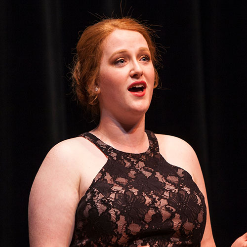 A woman dressed up with bright red hair singing passionately