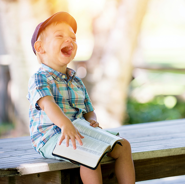 A young boy joyfully smiling with a book, could be a bible, on his lap