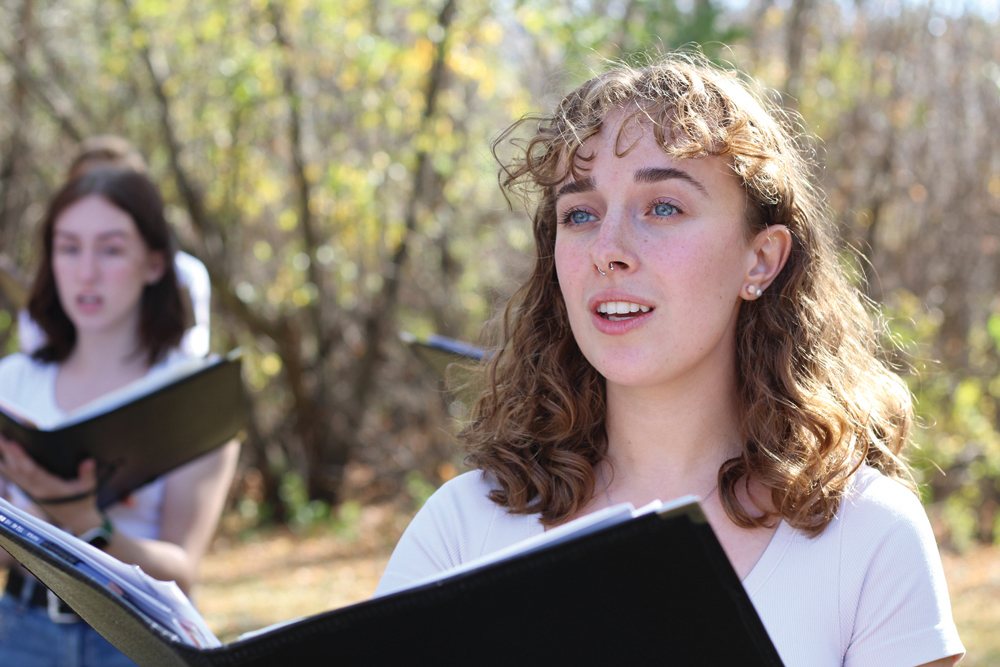 A person sings while holding a folder of sheet music