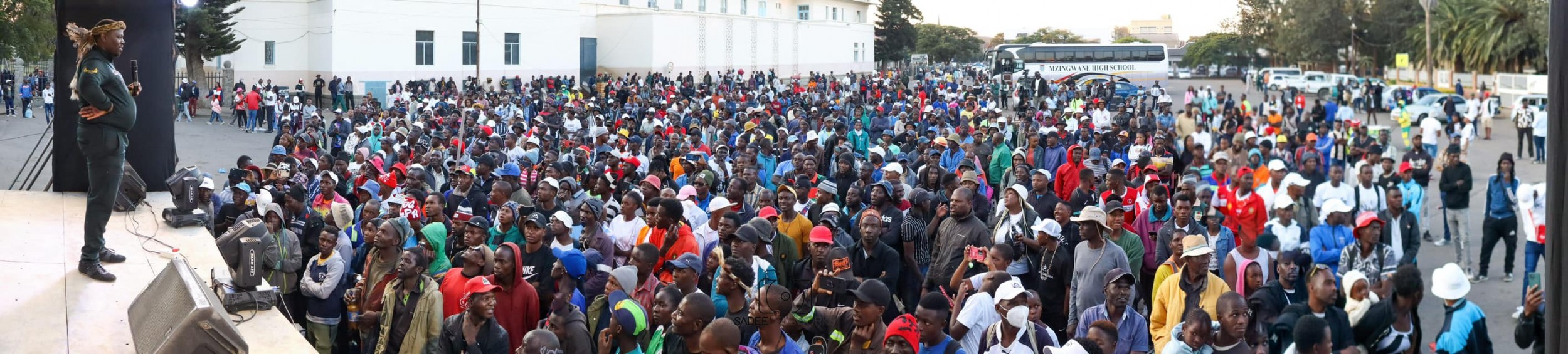 A wide horizontal side shot of concert stage with emcee, Madlela Skhobokhobo looking to a large crowd at the Bulawayo Arts Festival concert.
