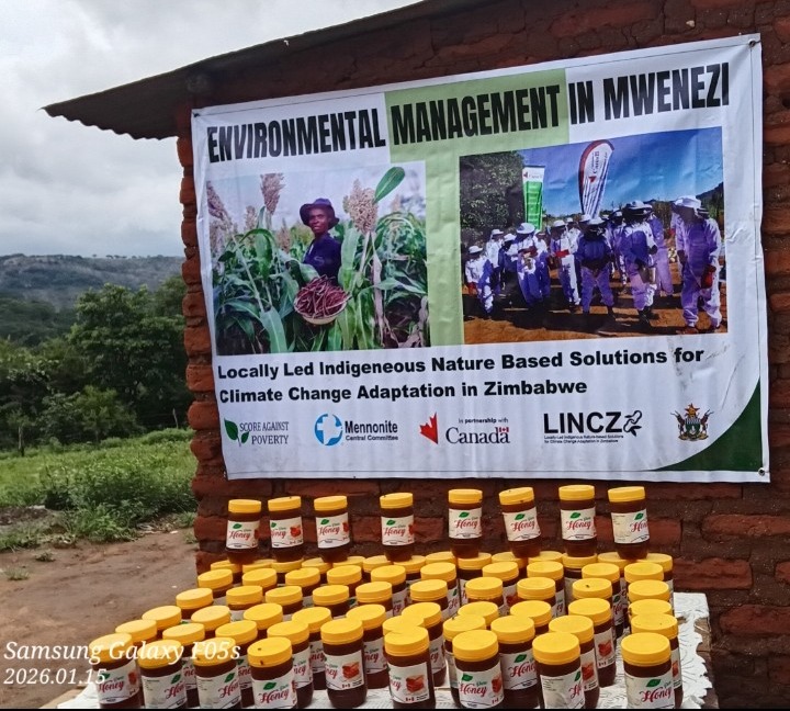 Simon's honey bottles for sale, displayed on a table outdoors in front of a banner that reads, "Environmental management in Mwenezi."