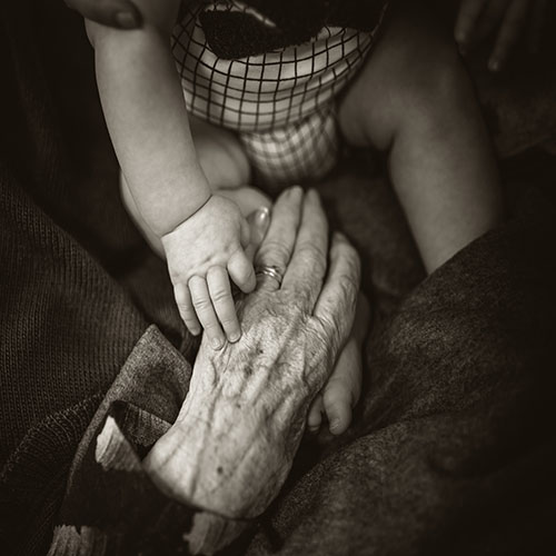 An older woman's hand holding the hand of a plump baby