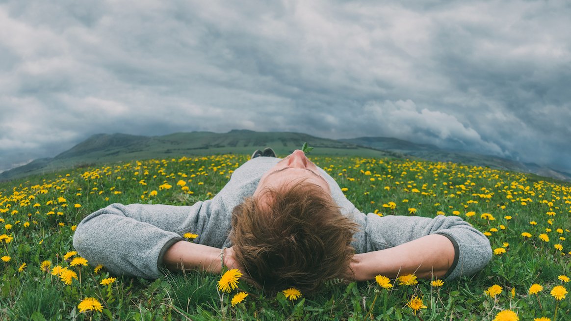 A man lying on a field of dandelions looking up at the sky