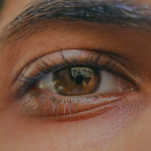 A striking brown eye of someone with brown skin, looking straight into the camera